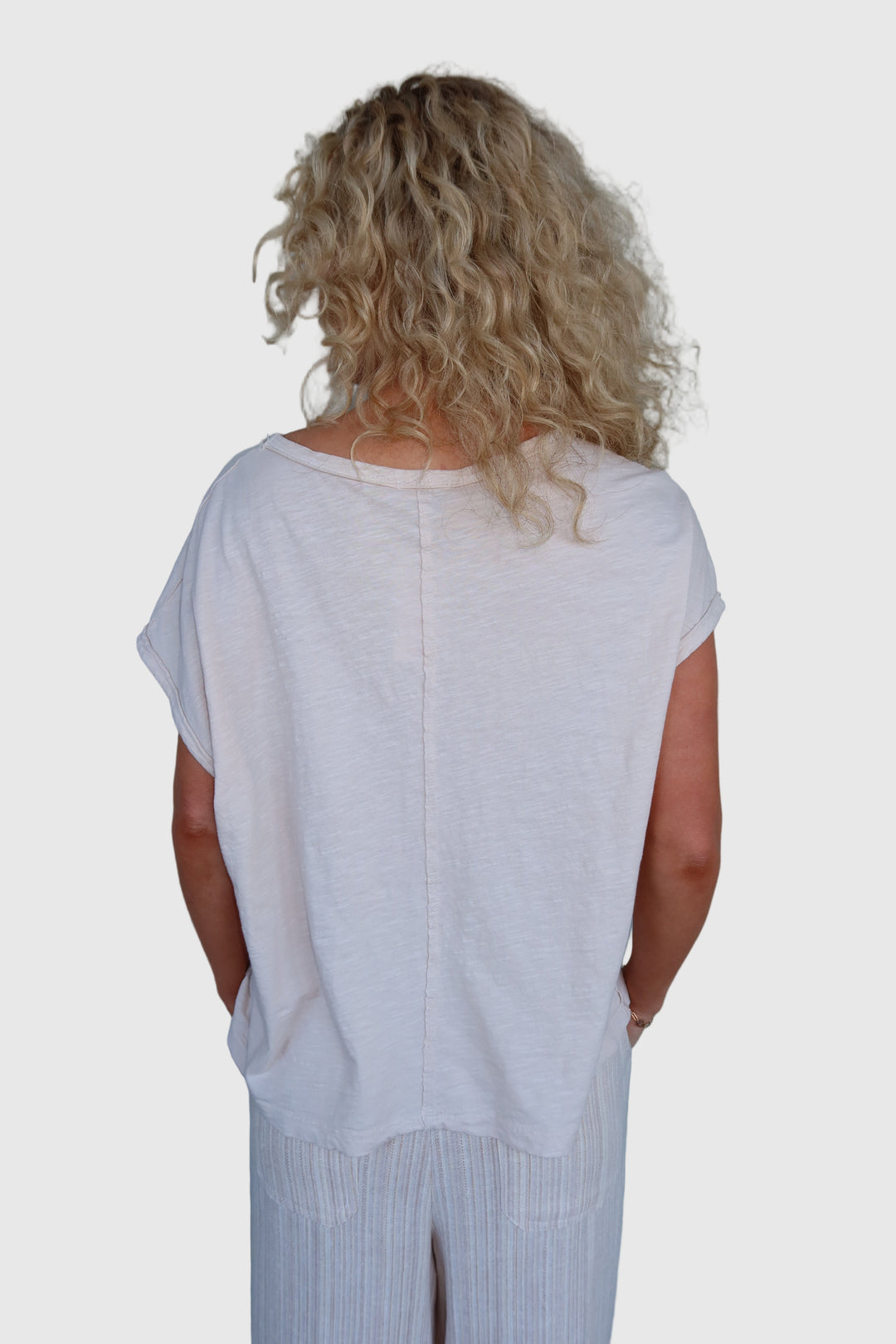 A woman wearing a Boxy Cap Sleeve Tee with a relaxed fit, paired with light-colored trousers