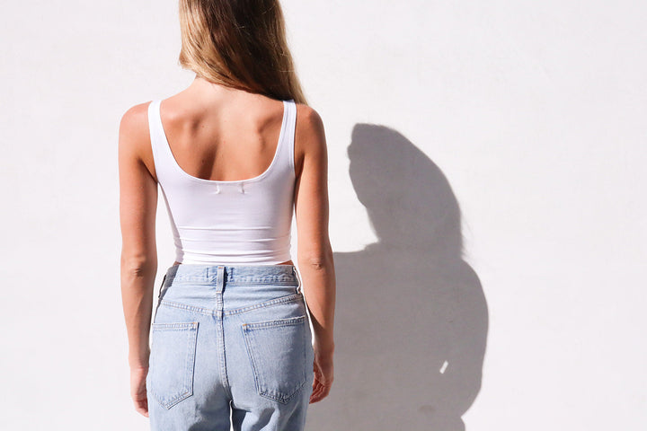 Product shot of NŪD Apparel Devon Double Layered Scoop Crop top in white paired with light wash denim, back view.