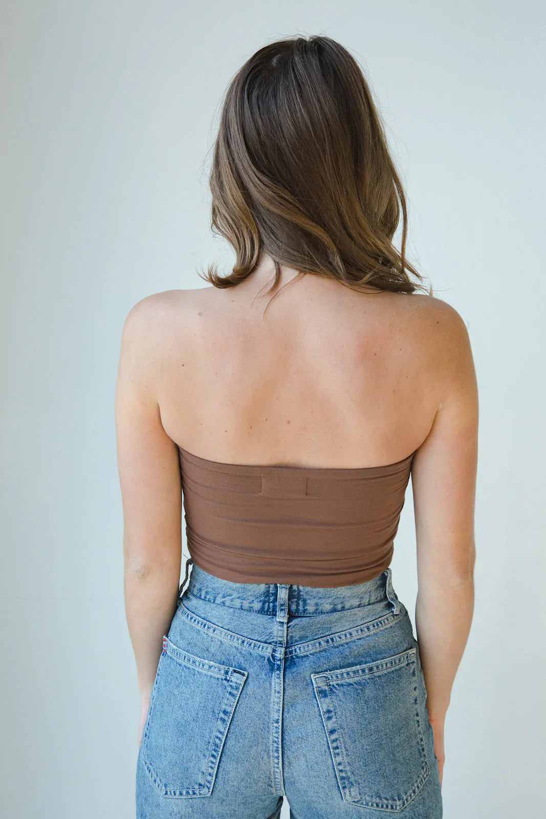 Product shot of NŪD Apparel Hunter Double Layer Bandeau in dark nude paired with high rise denim, back view.
