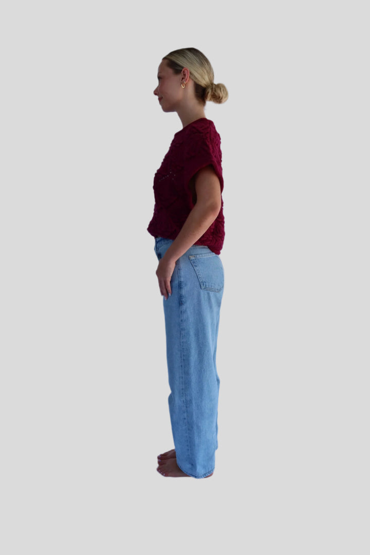 Person wearing a sweater top and light blue jeans standing against a white background