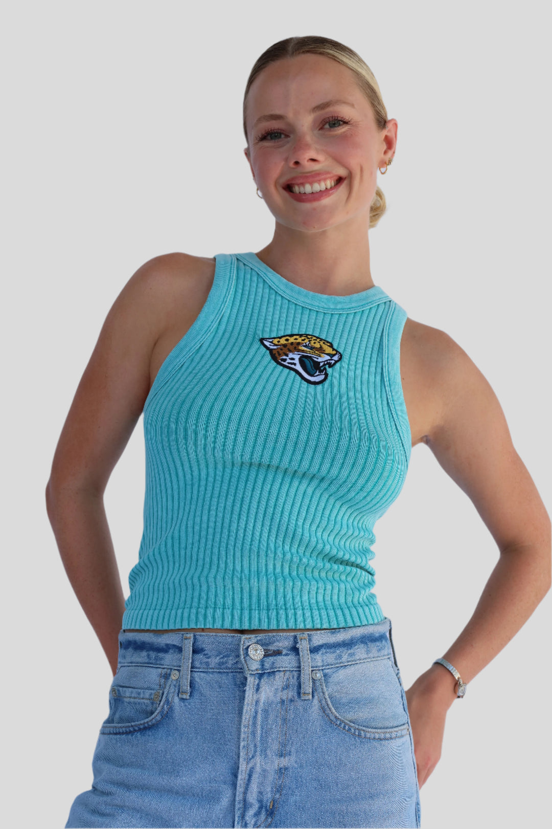 Woman wearing a turquoise ribbed tank top with a Jaguar logo and denim against a white background.