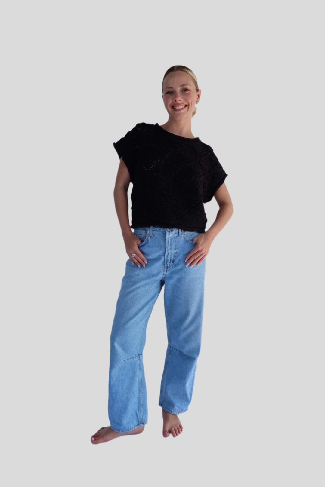 Person wearing a black top and blue jeans against a light background