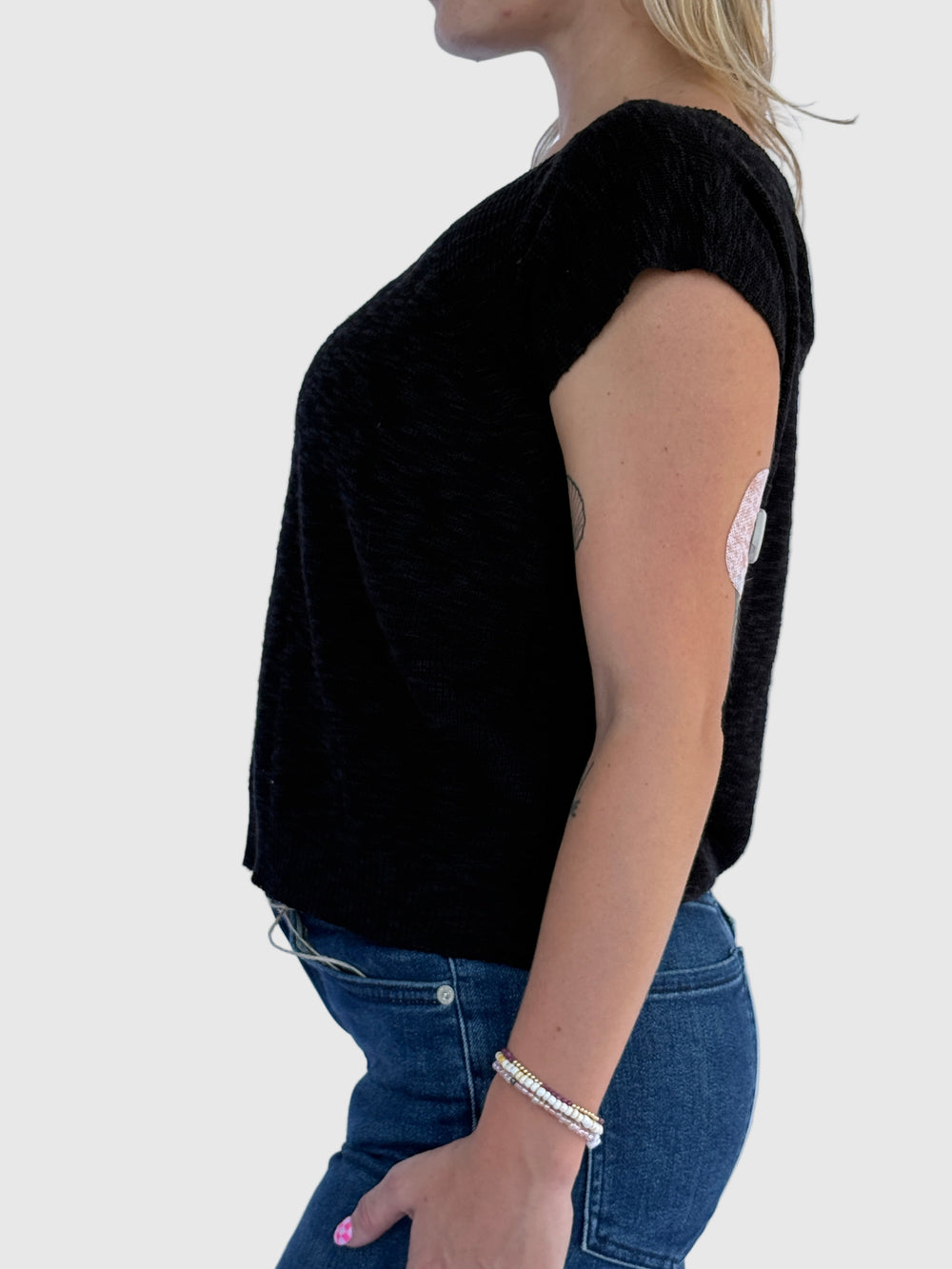 Person wearing a black top and blue jeans against a light background