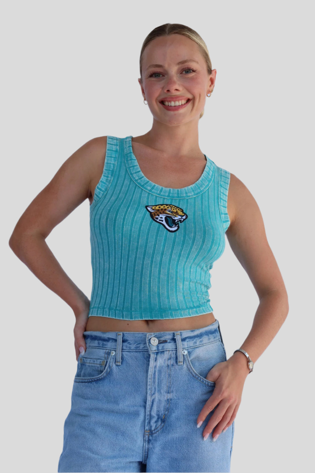 Woman wearing a turquoise ribbed tank top with a Jaguar logo and blue jeans against a light background