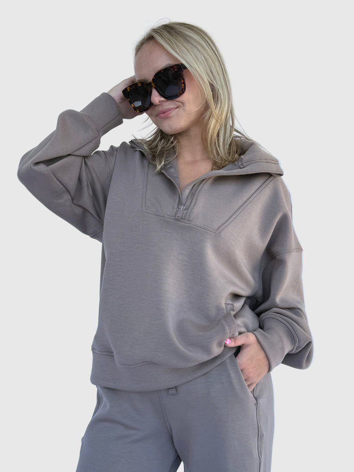 Person wearing a gray outfit with sunglasses against a light background