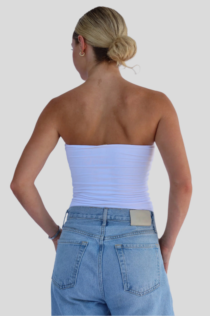 Person wearing a white strapless top and blue jeans against a light background