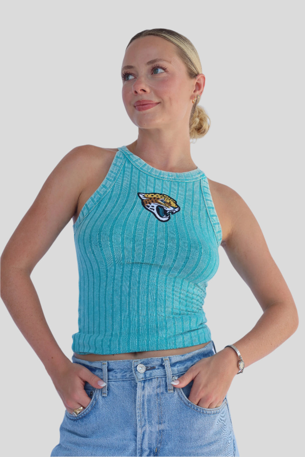 Woman wearing a turquoise ribbed tank top with a Jaguar logo and blue denim shorts against a light background