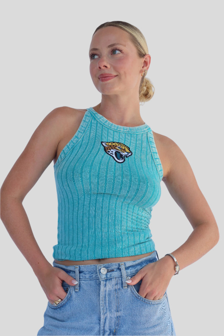 Woman wearing a turquoise ribbed tank top with a Jaguar logo and blue denim shorts against a light background