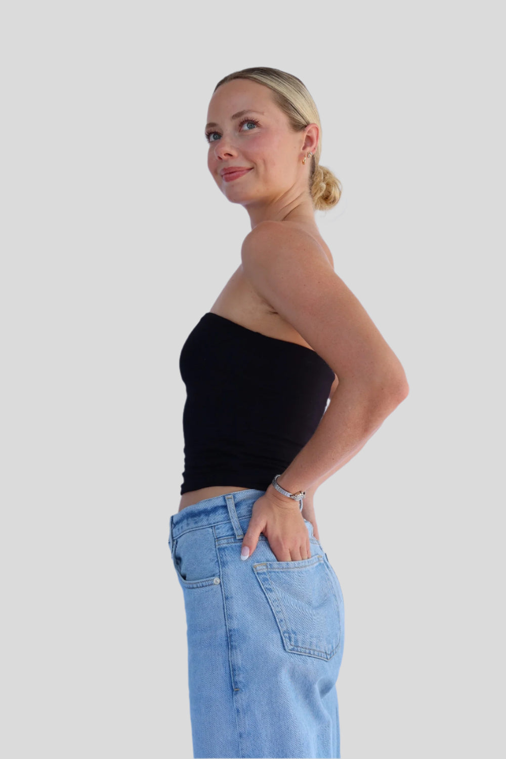 Woman wearing a black strapless top and blue jeans against a light background