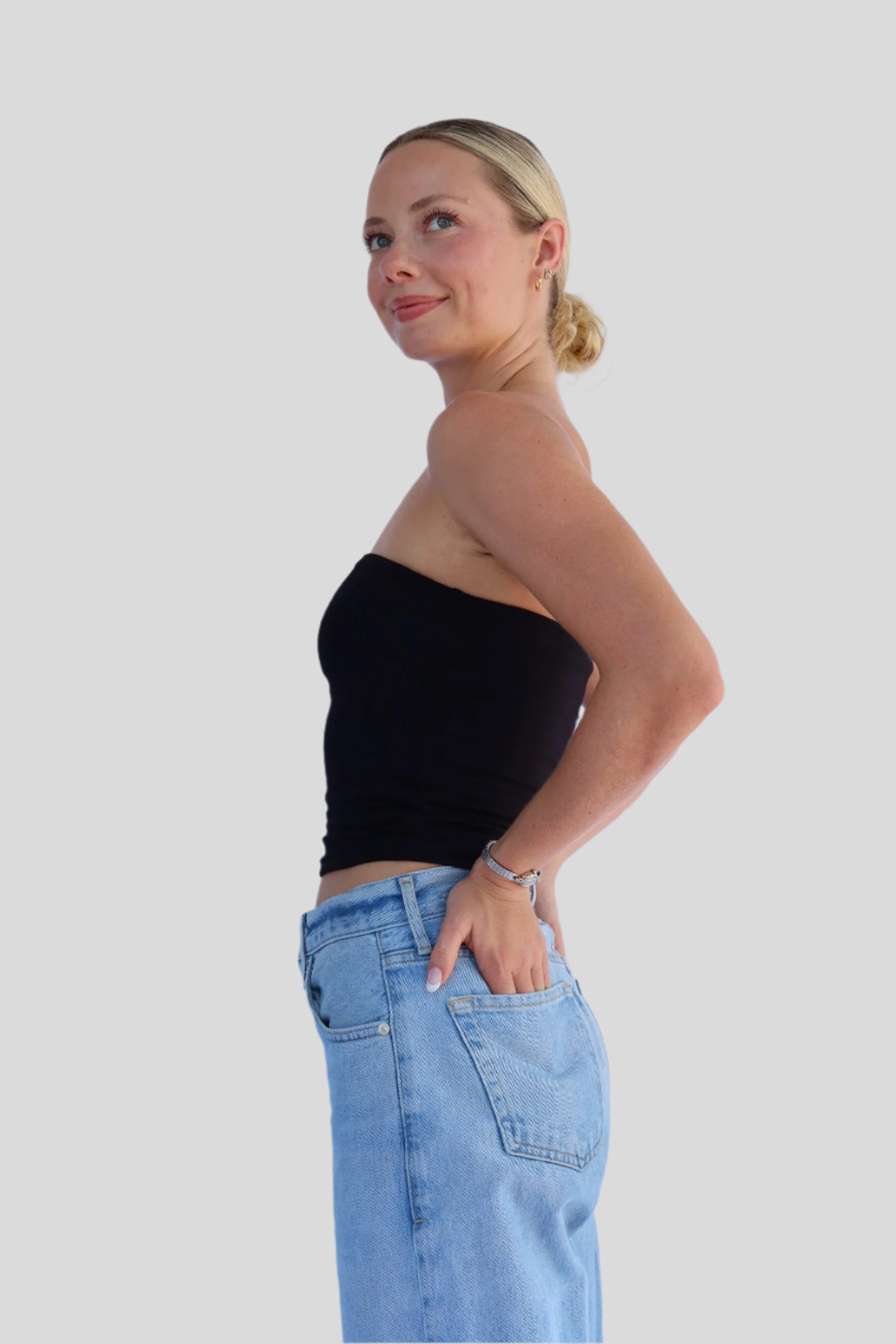 Woman wearing a black strapless top and blue jeans against a light background