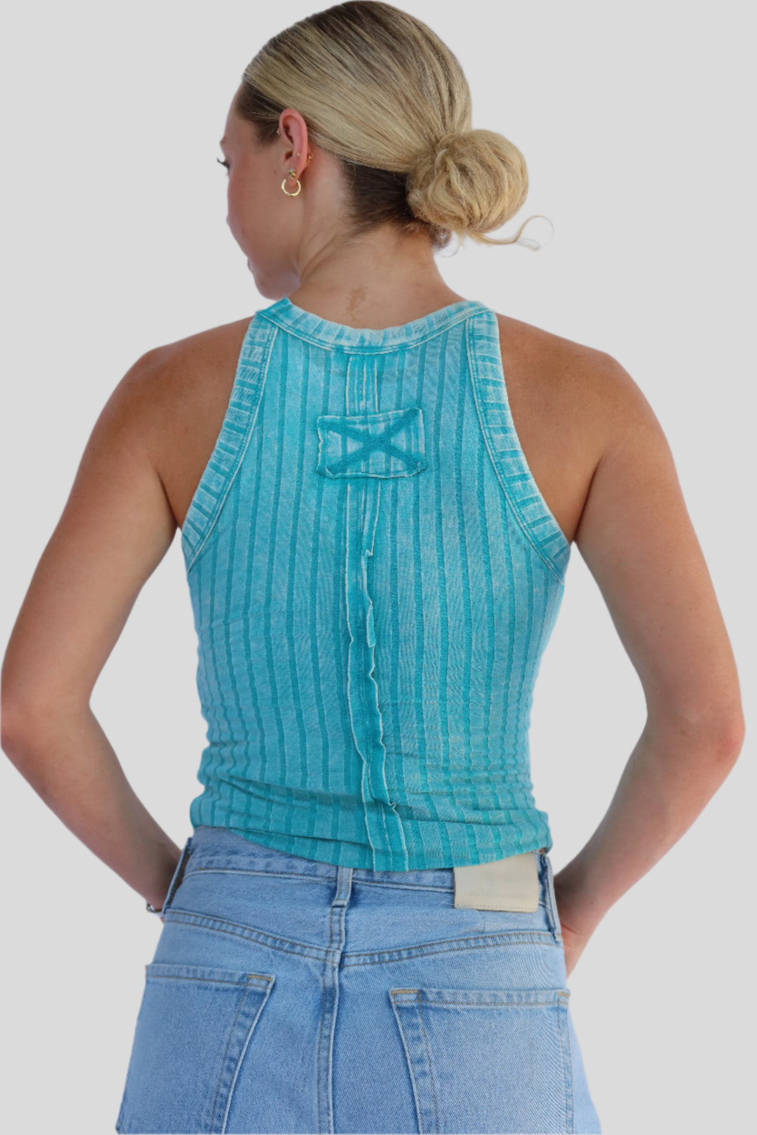 Woman wearing a turquoise sleeveless top and blue jeans against a light background