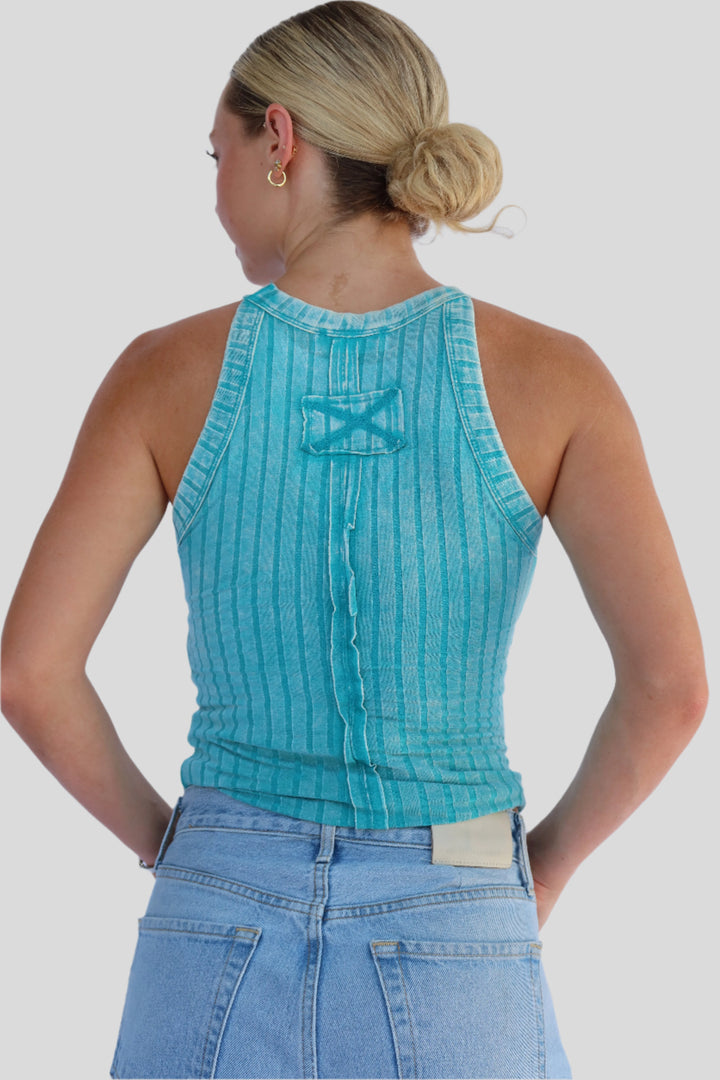 Woman wearing a turquoise sleeveless top and blue jeans against a light background