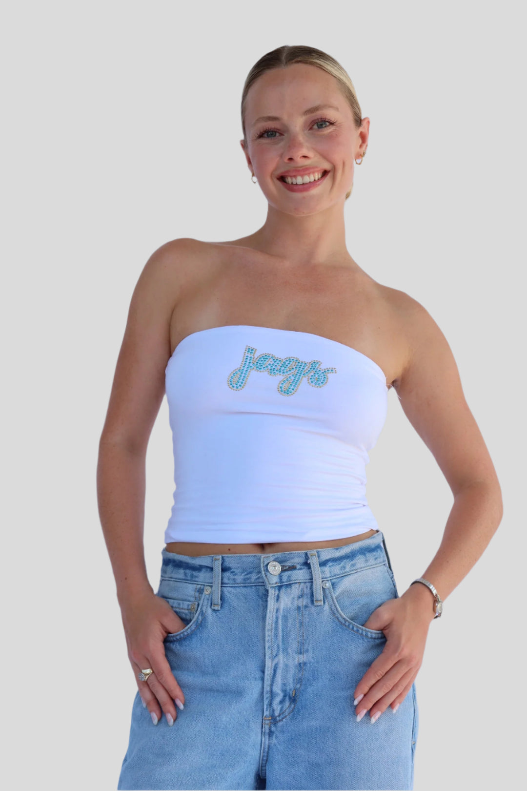 Woman wearing a strapless top with 'Jags' text and jeans against a light background