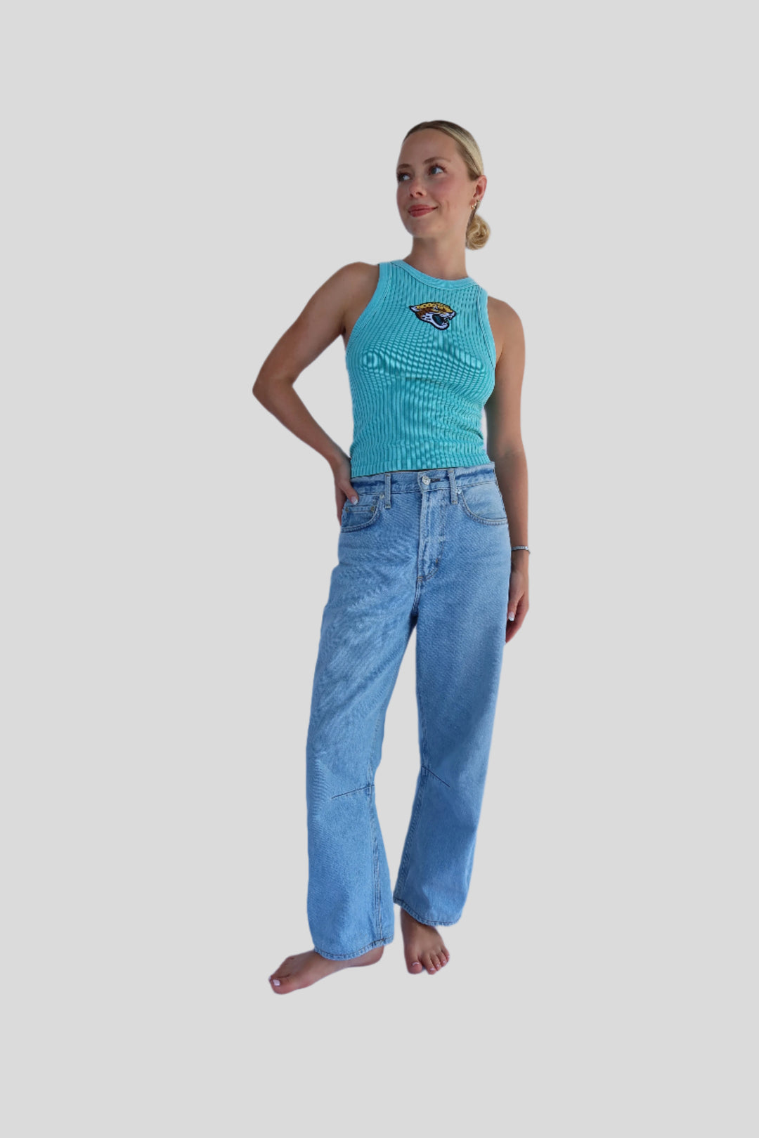 Person wearing a turquoise tank top and blue jeans against a light blue background