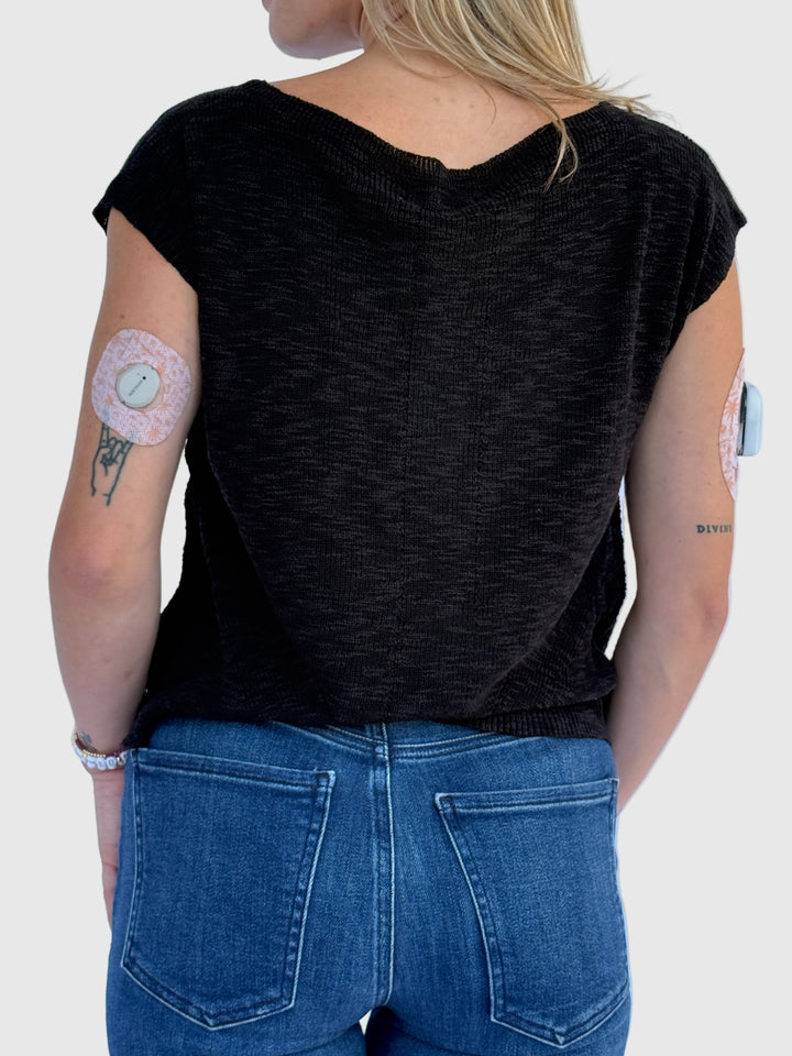 Person wearing a black sleeveless top and blue jeans against a light background