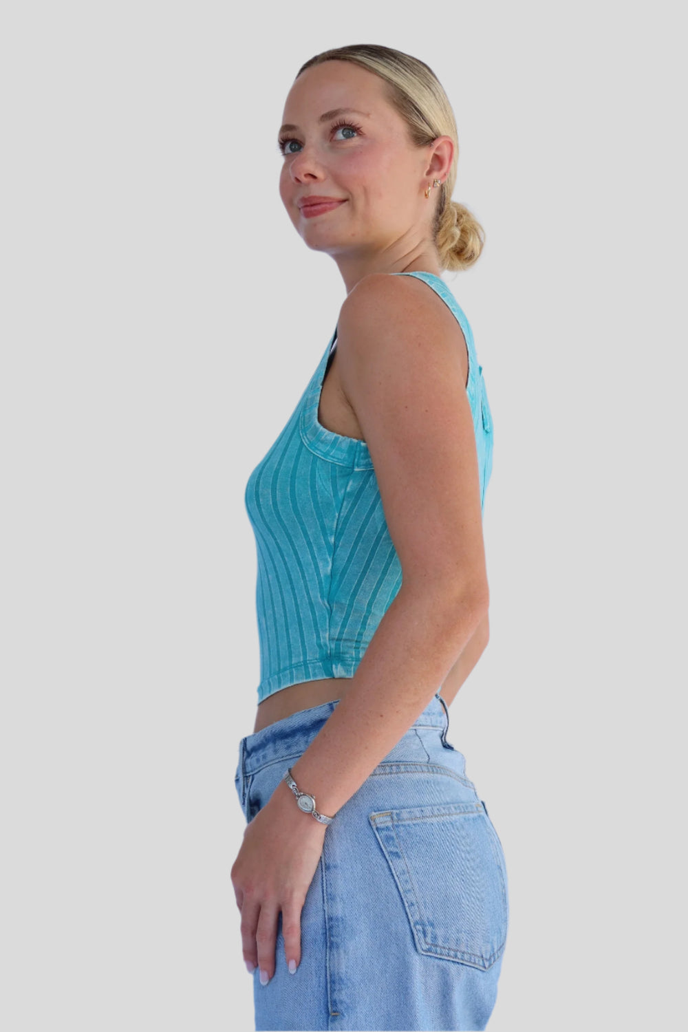 Woman wearing a turquoise tank top and light blue jeans against a light background