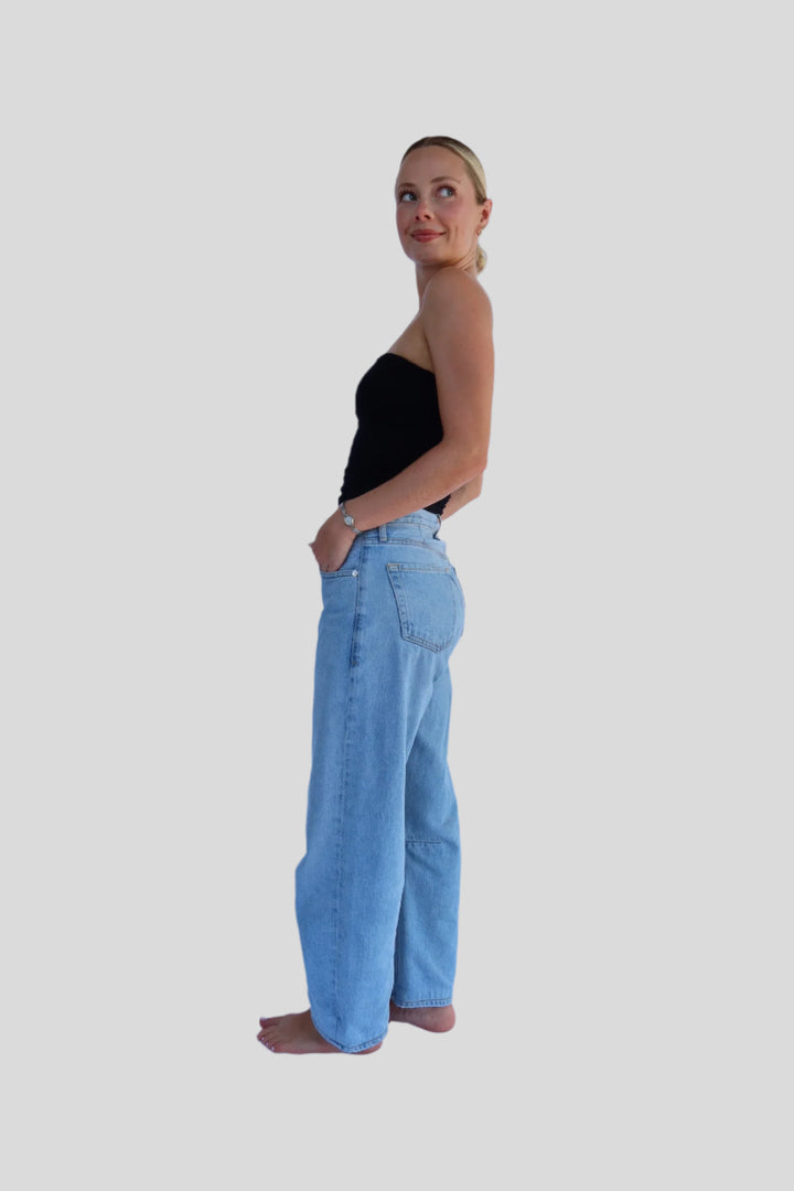 Woman wearing a black top and light blue jeans on a white background