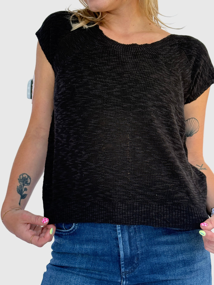 Person wearing a black sleeveless top and blue jeans on a light background