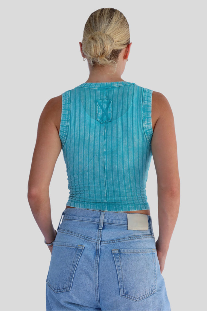 Person wearing a turquoise sleeveless top and blue jeans against a light background