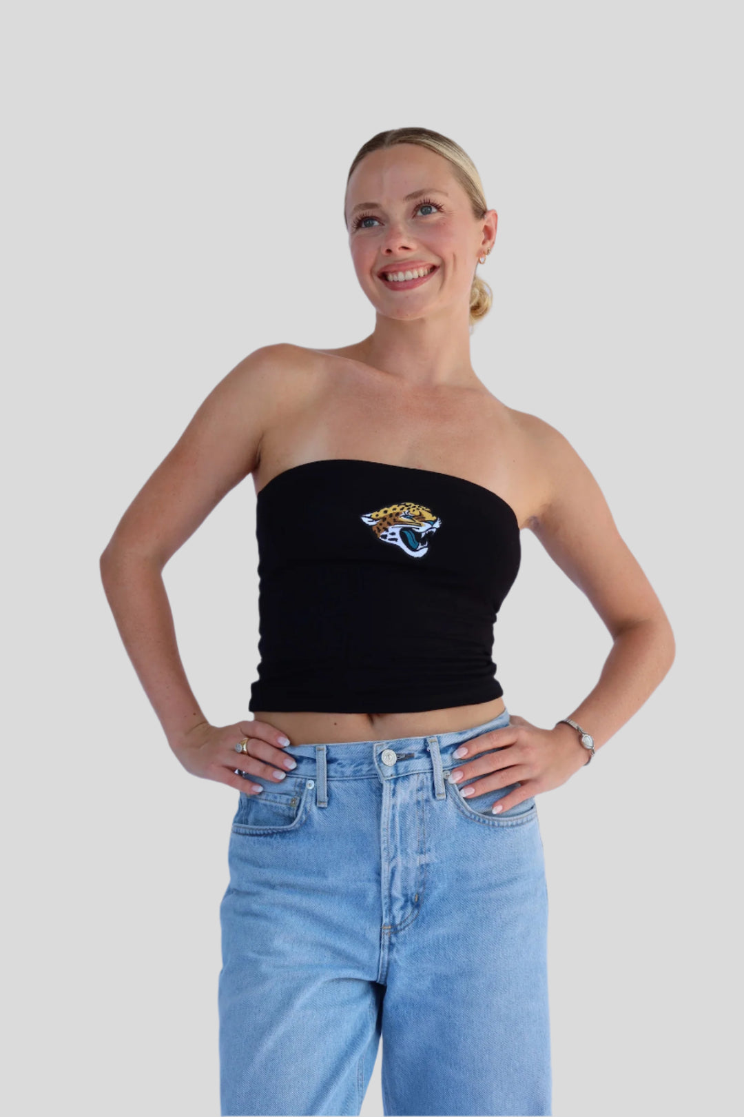 Woman wearing a black strapless top with a Jaguar logo and blue jeans on a plain background