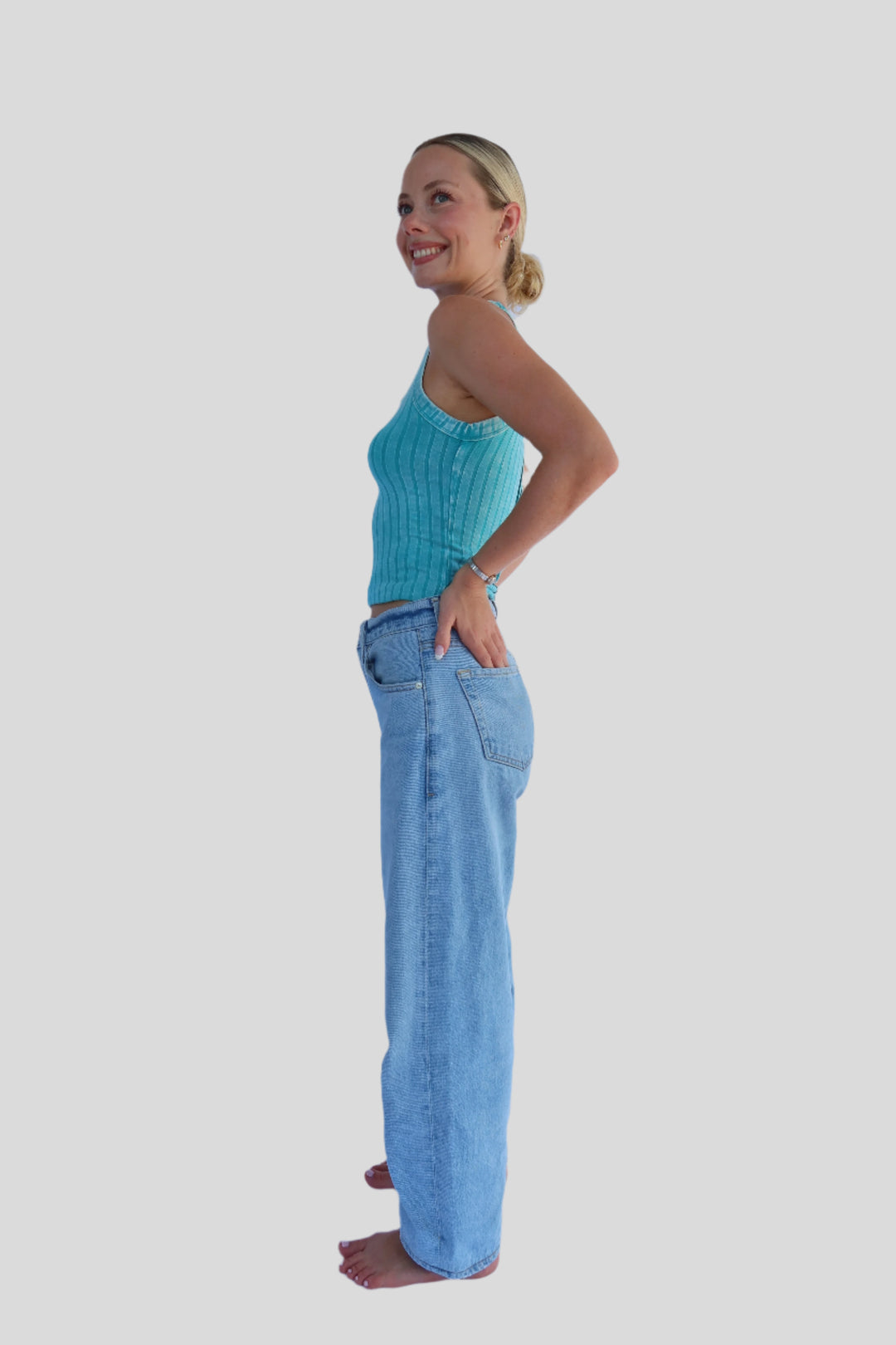 Person wearing a turquoise blue crop tank and jeans against a light background