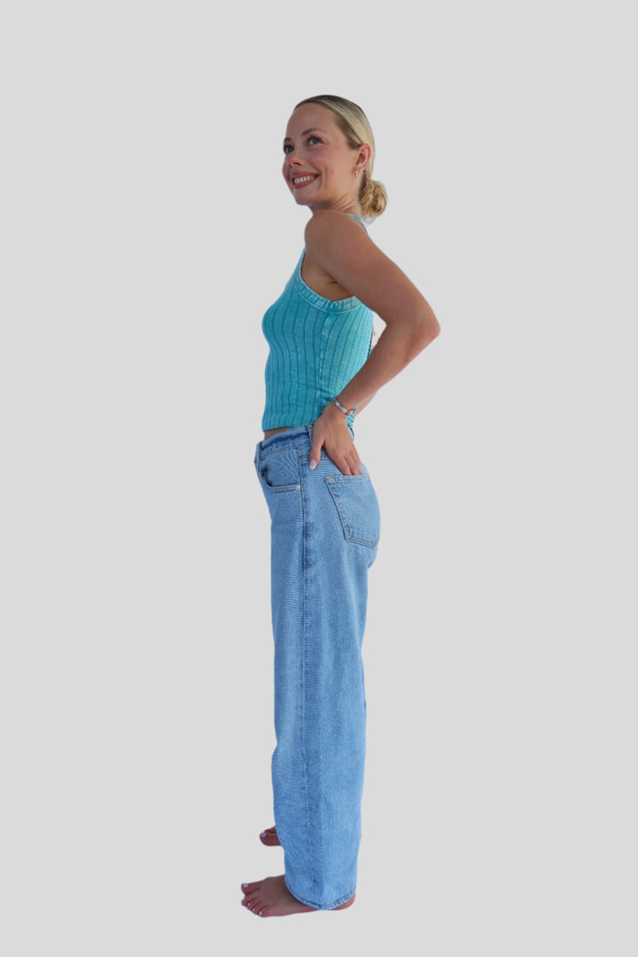 Person wearing a turquoise blue crop tank and jeans against a light background