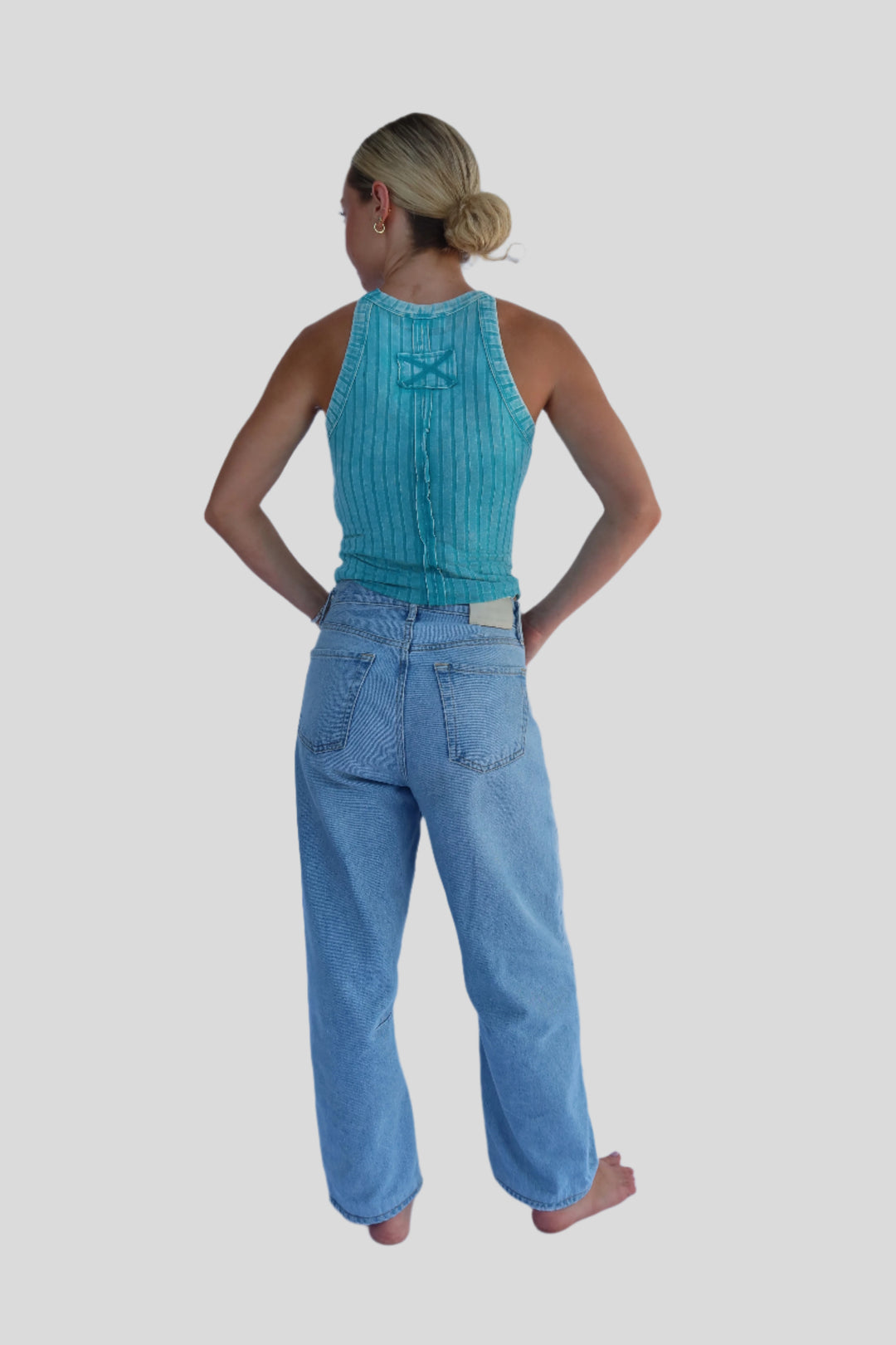 Person wearing a turqoise blue top and jeans against a light background