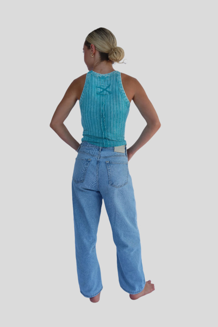 Person wearing a turqoise blue top and jeans against a light background
