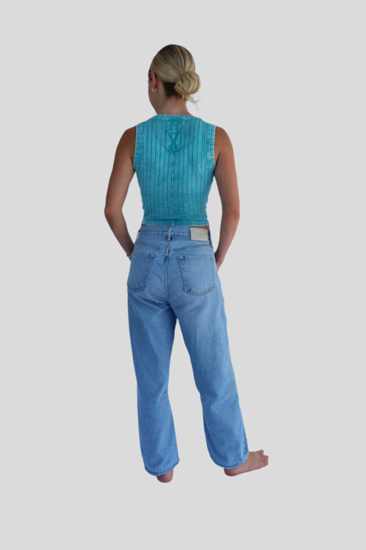 Person wearing a turquoise sleeveless top and light blue jeans on a white background