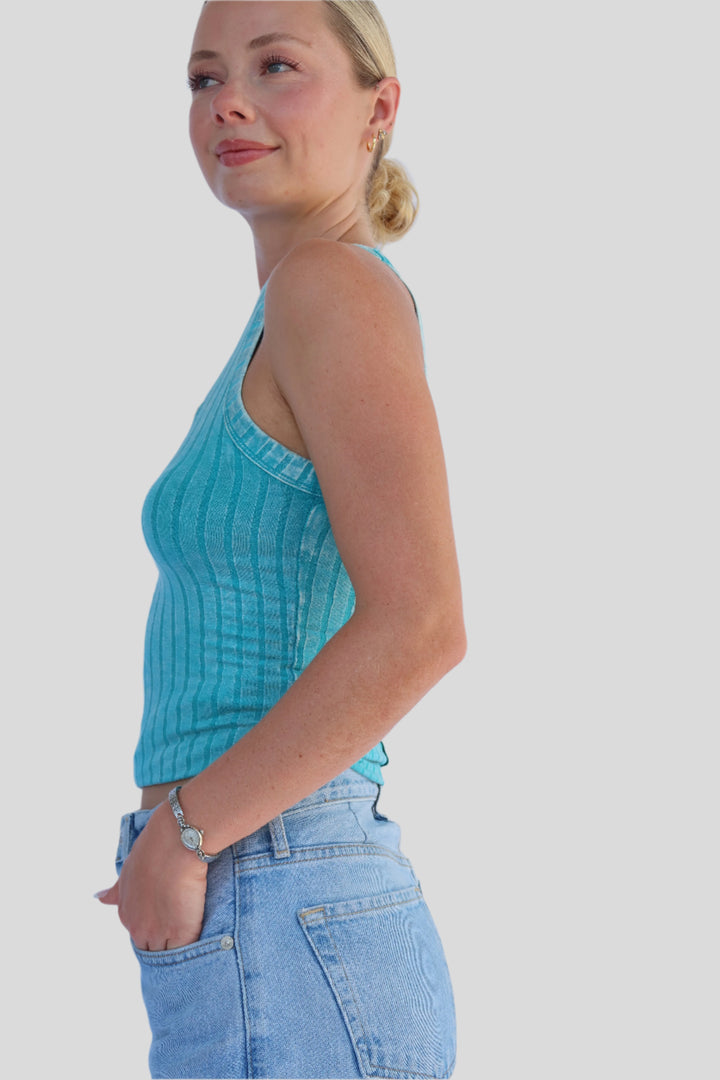 Woman wearing a turquoise top and blue jeans against a light background