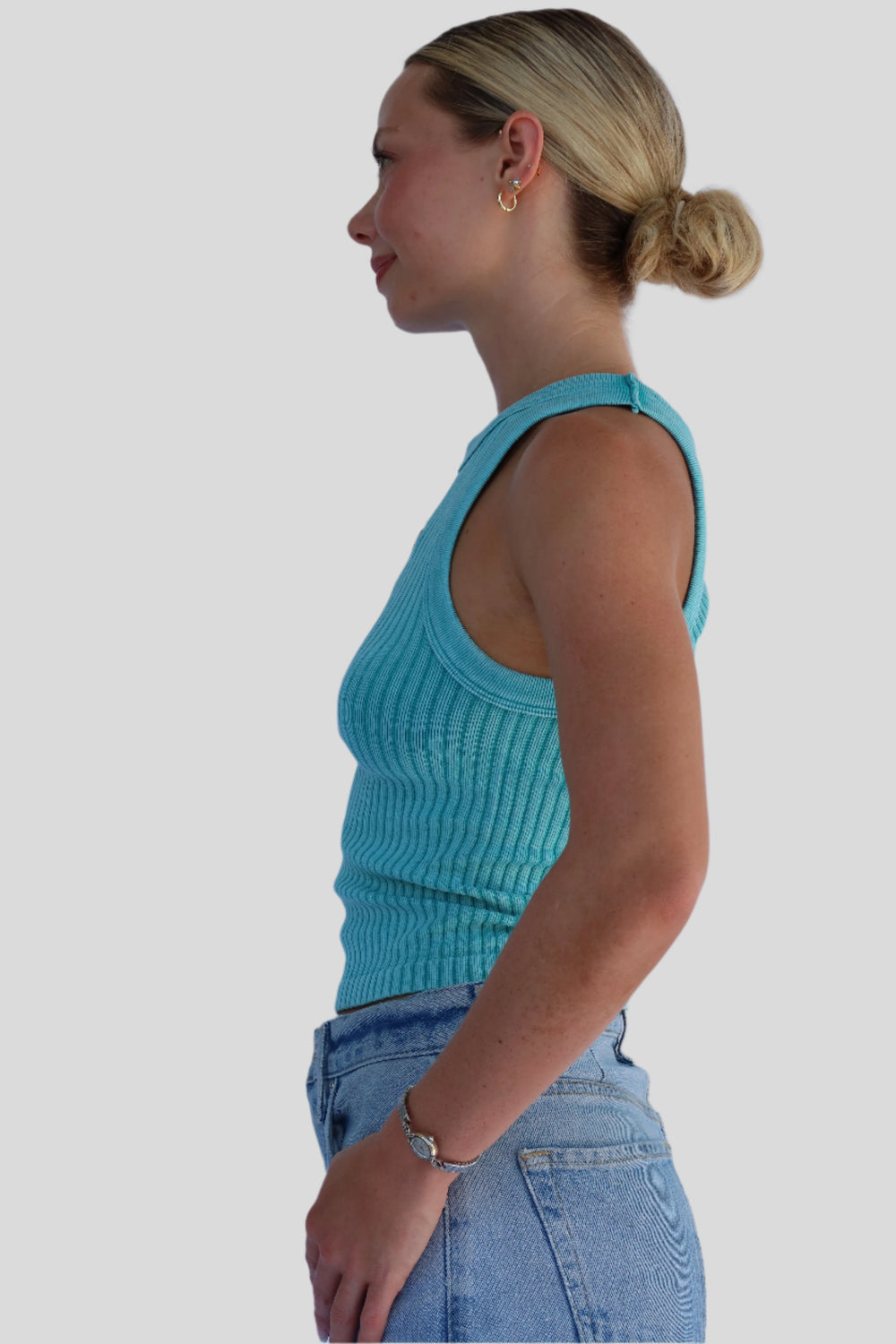 Person wearing a turquoise tank top and blue jeans against a white background.