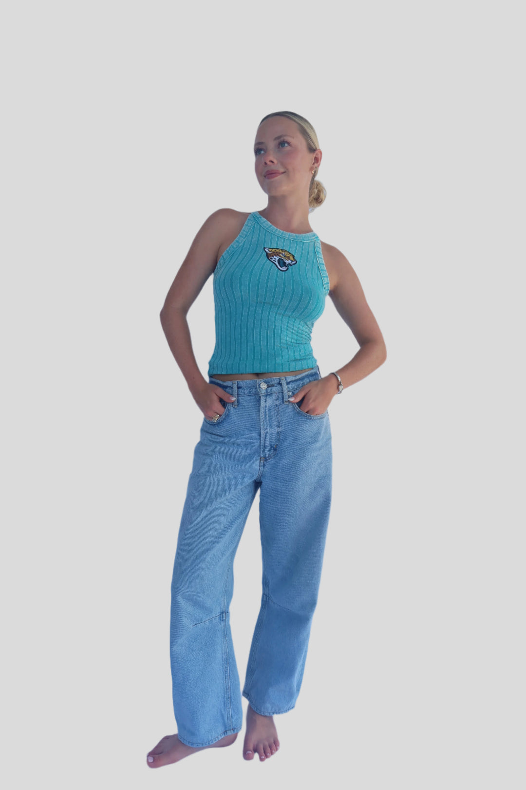 Person wearing a turquoise sleeveless top and light blue jeans against a white background