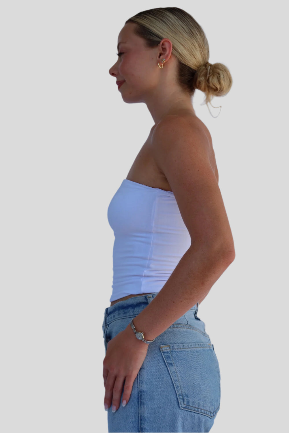 Woman wearing a white strapless top and blue jeans against a light background
