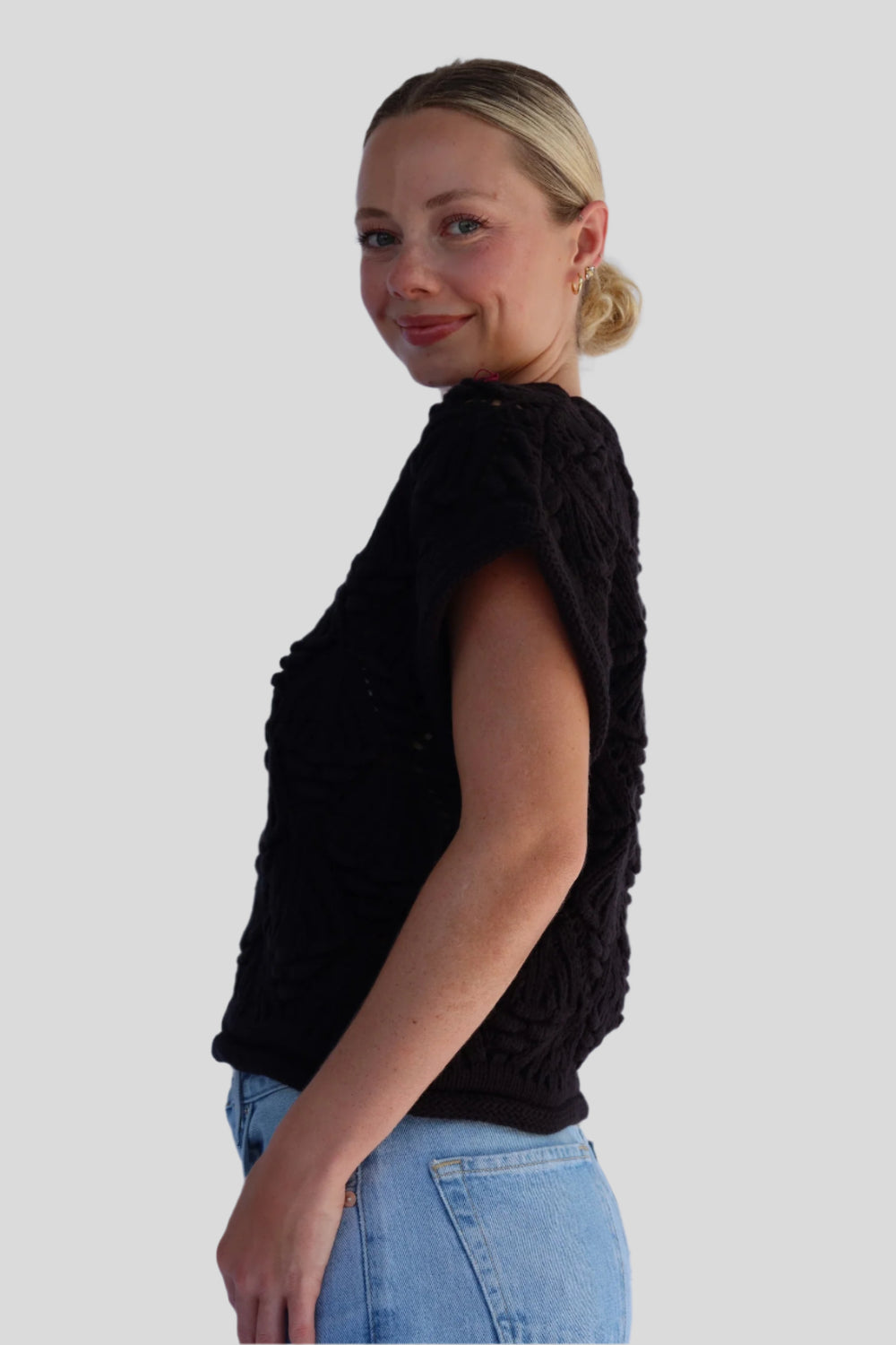 Woman wearing a black sleeveless top and blue jeans on a plain background