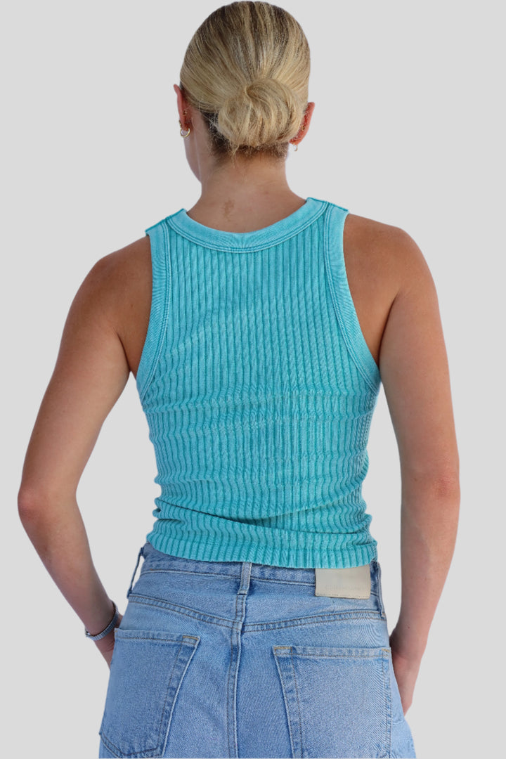 Person wearing a turquoise ribbed tank top and blue jeans against a light background