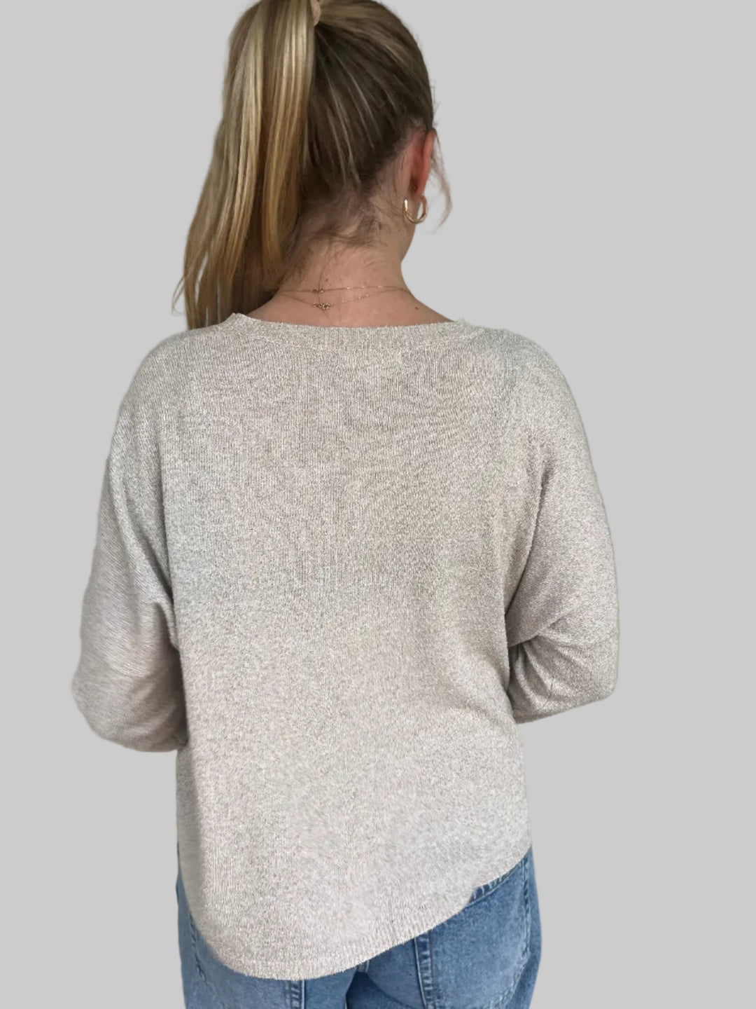 Back of person wearing tan knit top against a light grey wall 