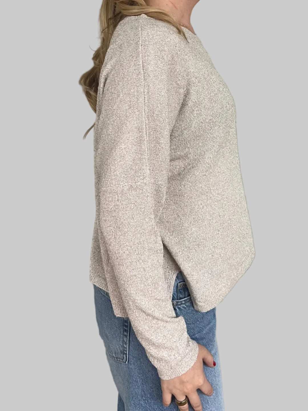 Side of person wearing tan sweater against a light grey wall.