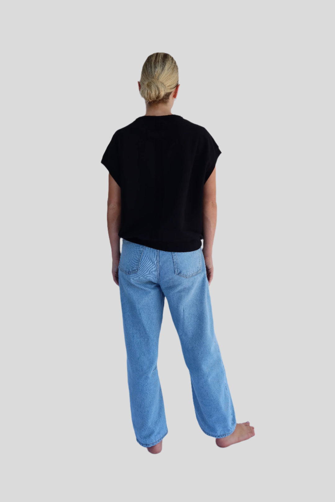 Person wearing a black top and blue jeans against a light background