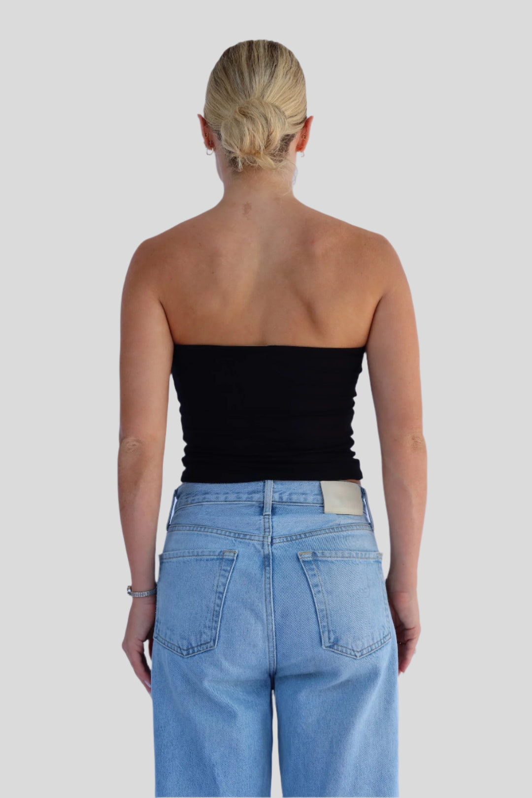Person wearing a black strapless top and light blue jeans against a light background