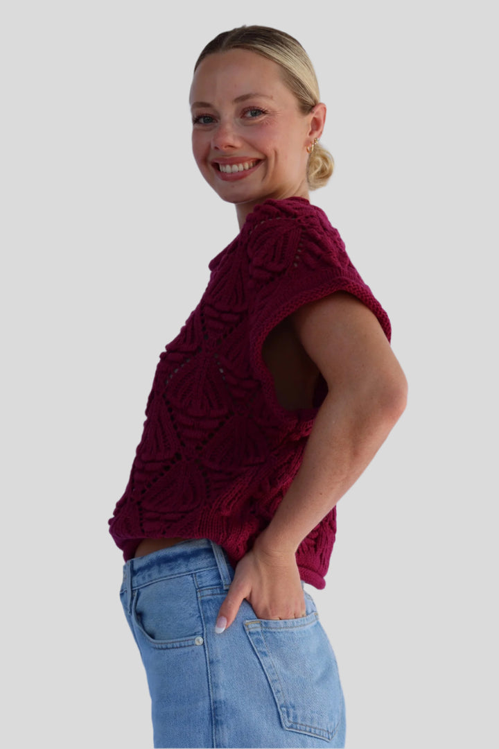 Woman wearing a burgundy knitted top and blue jeans against a neutral background