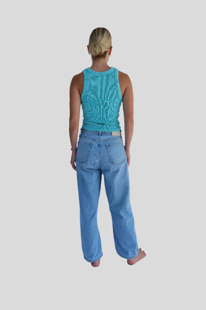 Person wearing a turquoise top and blue jeans against a light background