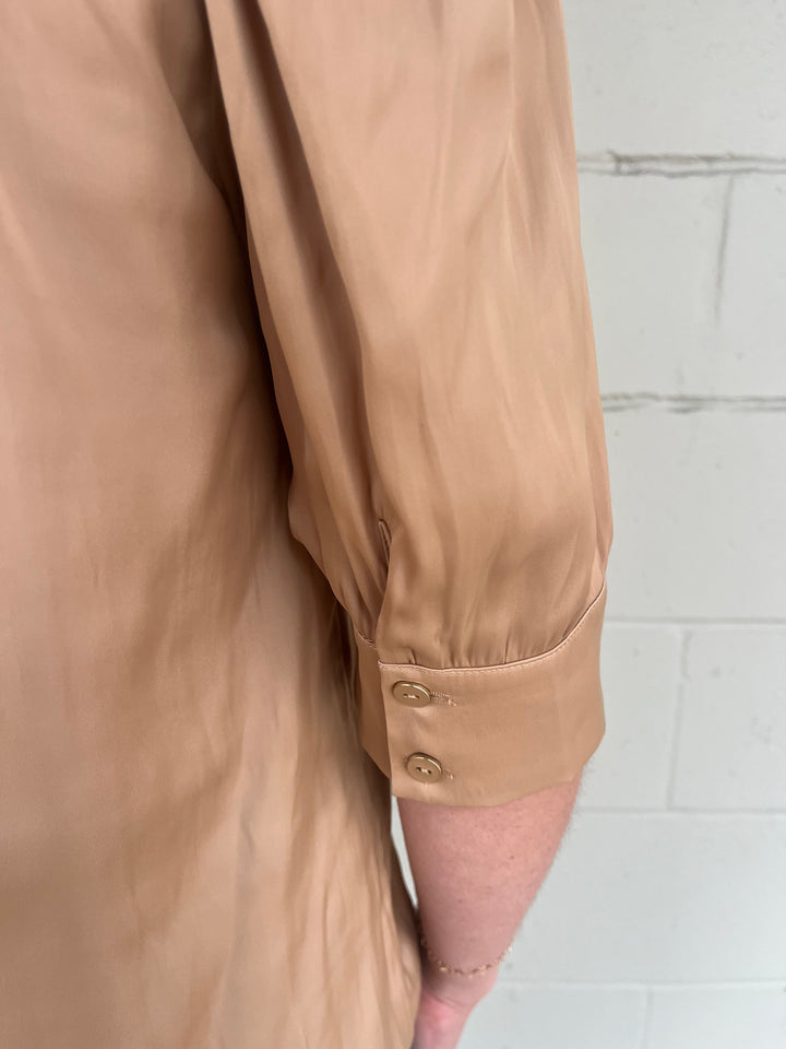 Close-up of a bronze satin shirt with sleeve against a gray wall.