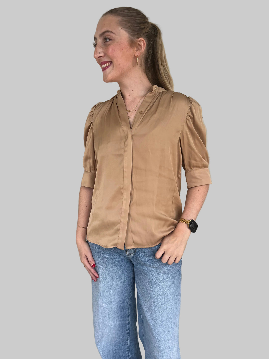 Person wearing a bronze top and blue jeans standing against a gray wall.