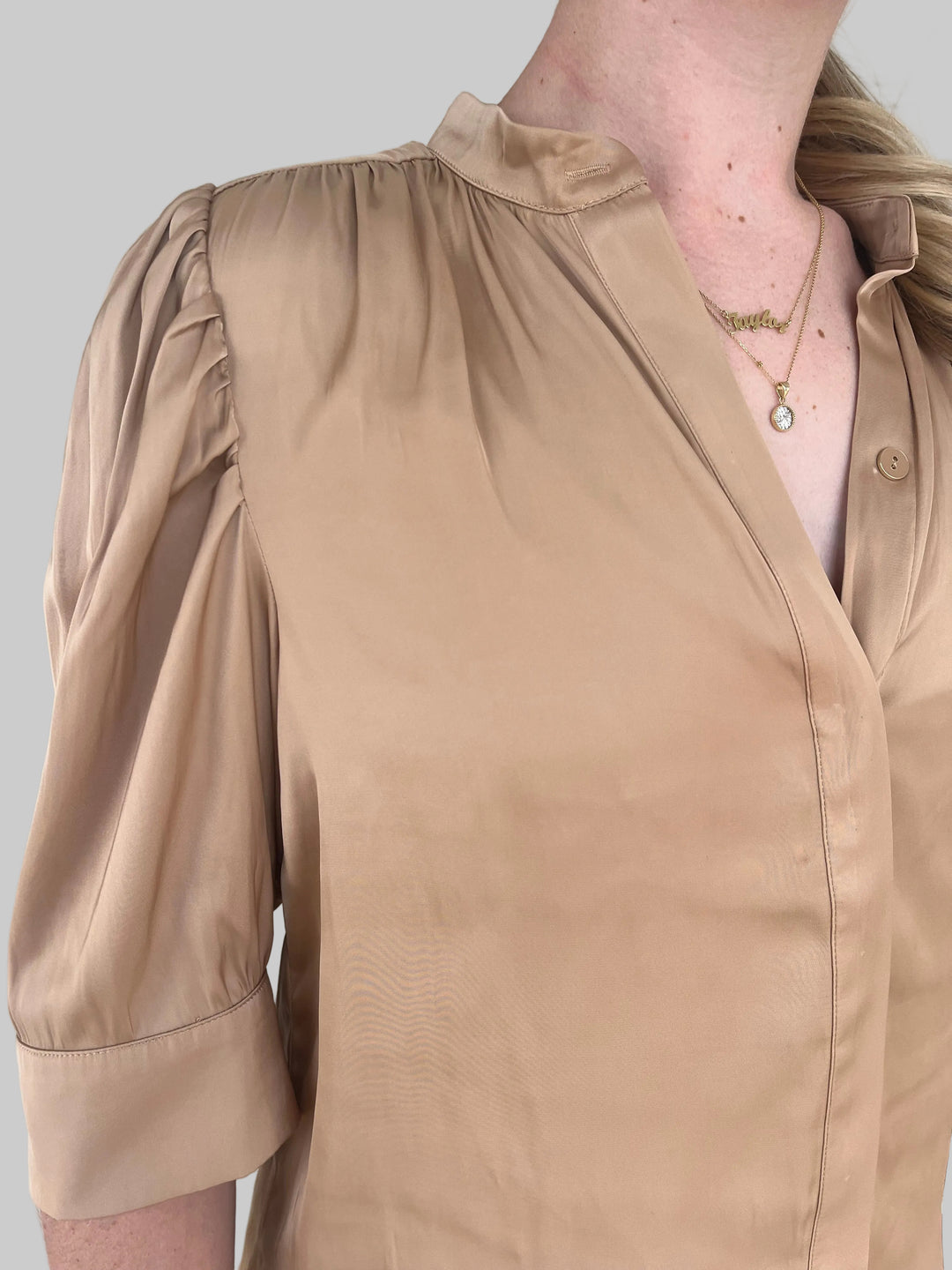 Close-up of a person wearing a bronze satin shirt with a light gray background