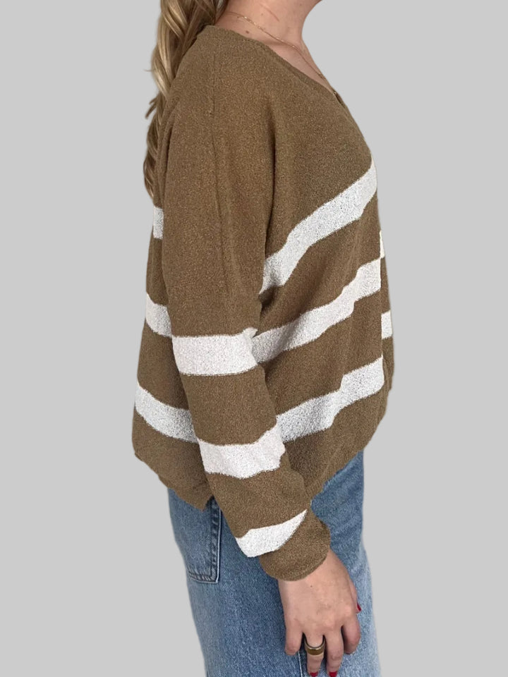Person wearing a brown sweater with white stripes on a light gray floor.