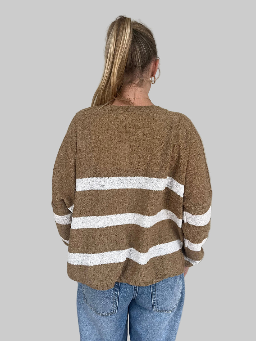 Person wearing a brown sweater with white stripes on a light wooden floor.