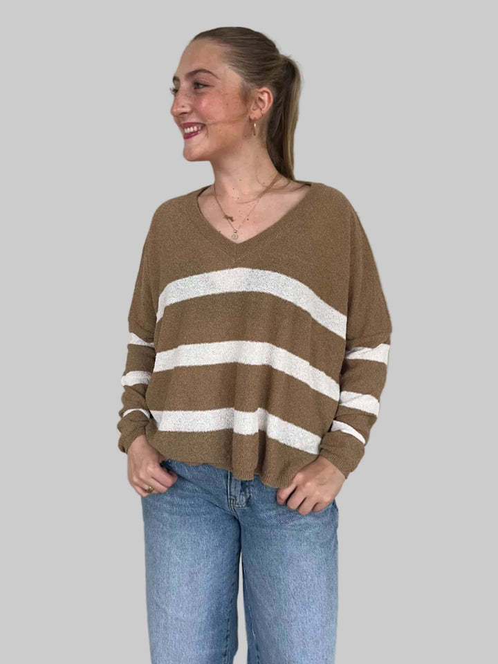 Person wearing a brown sweater with white stripes and blue jeans on a light wooden floor.