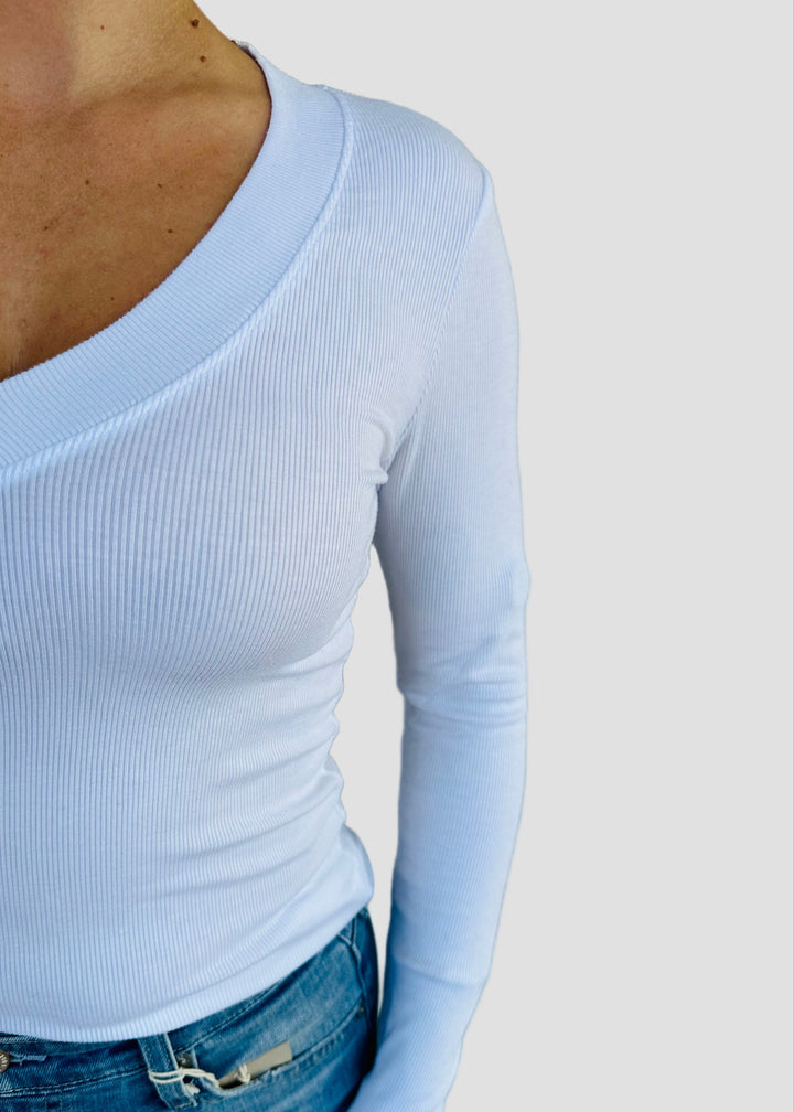 Person wearing a white long-sleeve top and blue jeans against a light green wall.