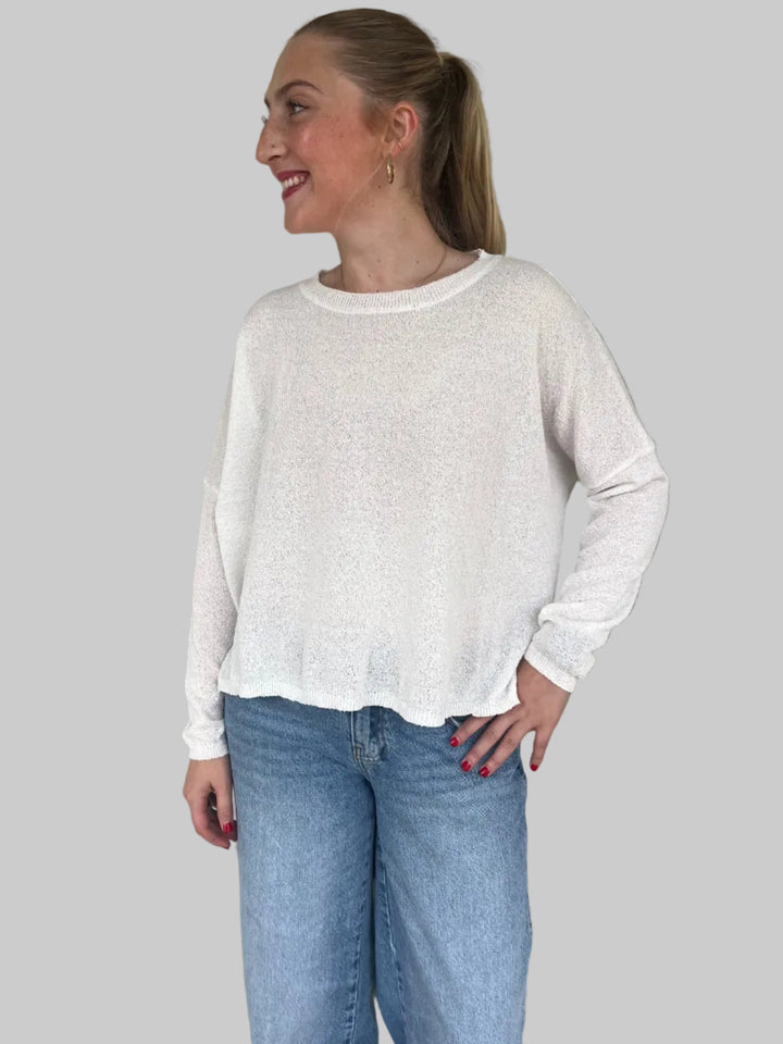 Person wearing a white long-sleeve knit top and blue jeans on a light gray floor.