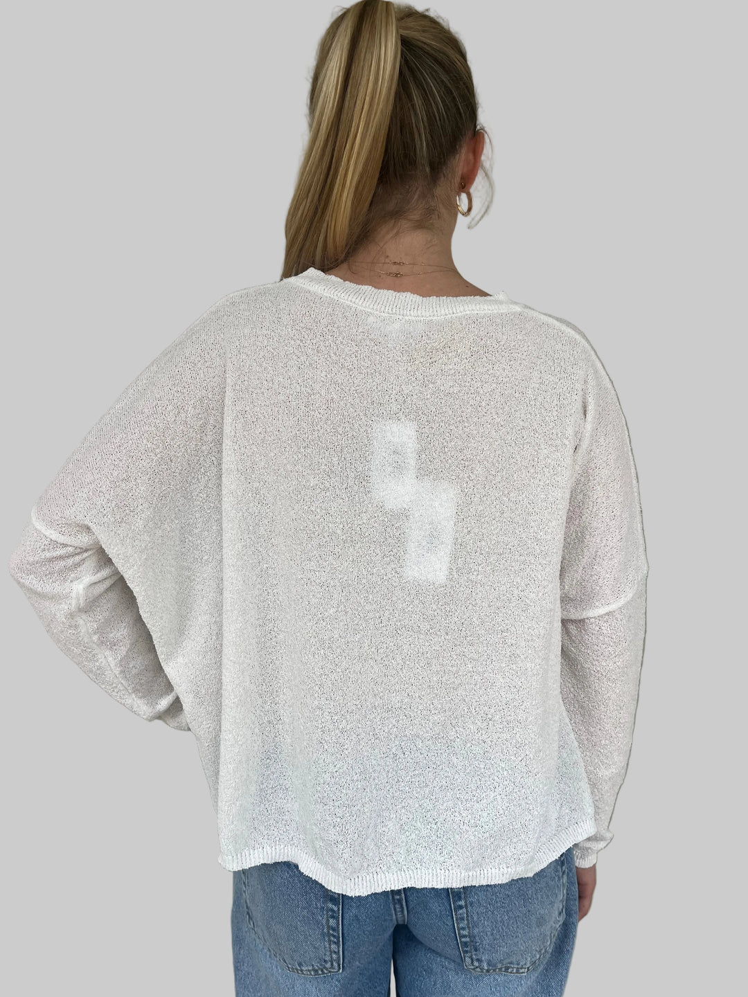 Person wearing a white textured knit top, standing against a light gray wall.